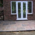 Paved patio area with white double-glazed door and windows in brick house.