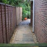 Garden pathway between wooden fence and brick wall for outdoor access.