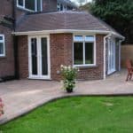 Extension with large glass doors and windows, outdoor patio area, and well-maintained garden space i.