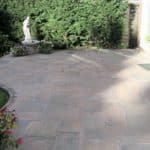 Garden patio with paving stones, statue, and garden hose reel.
