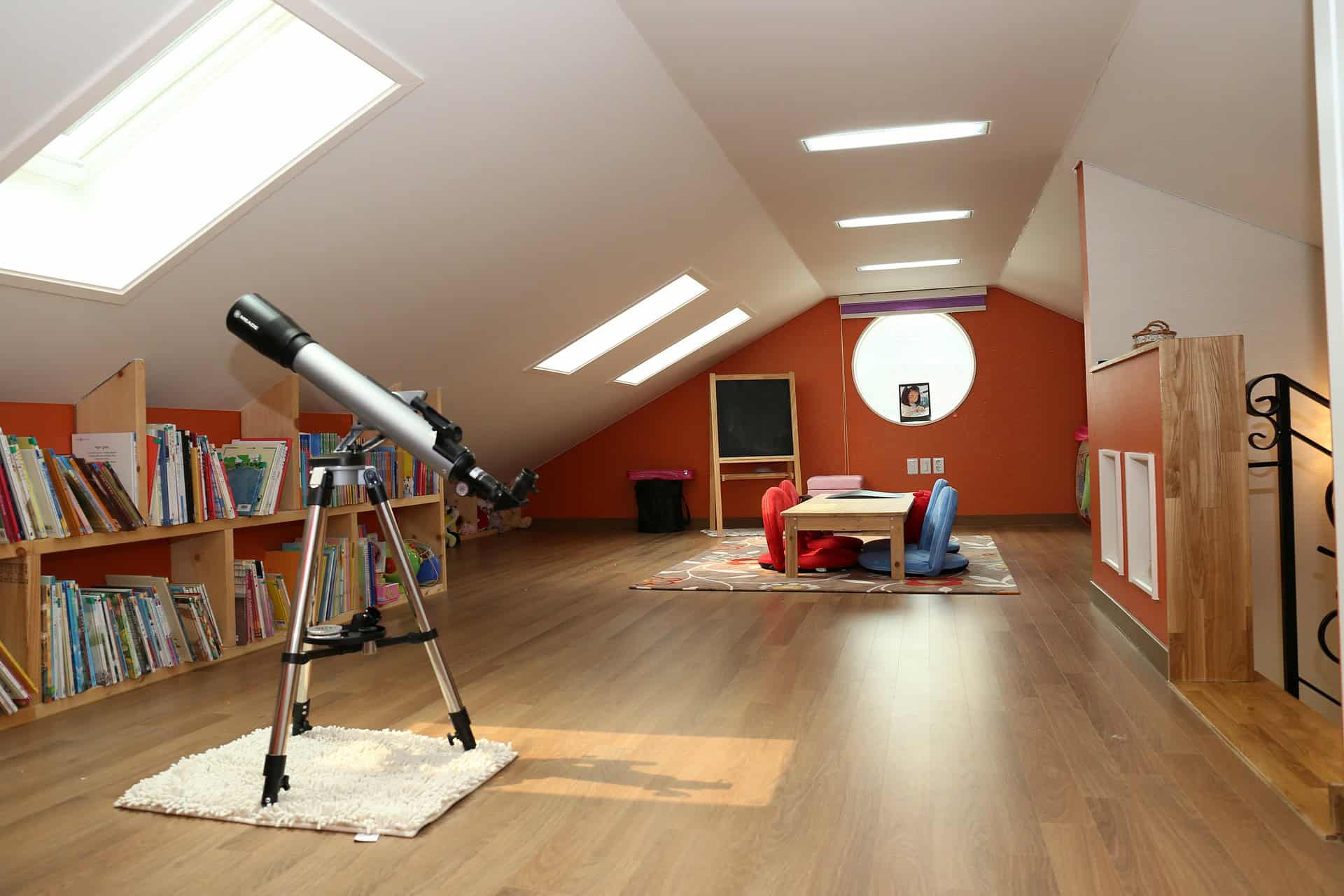 Modern attic space with telescope, bookshelves, and cosy seating area.