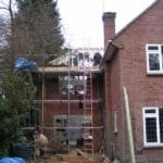 Construction workers building scaffolding on a brick house extension.