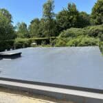 Flat roof installation by ConstrucTek in a lush green environment.