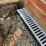 Drainage pipe and channel drain setup near brick wall.