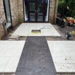 Porcelain patio with black brick pathway leading to glass doors, outdoor space renovation.