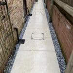 Porcelain patio pathway with drainage covers between brick walls, showcasing durable outdoor paving.