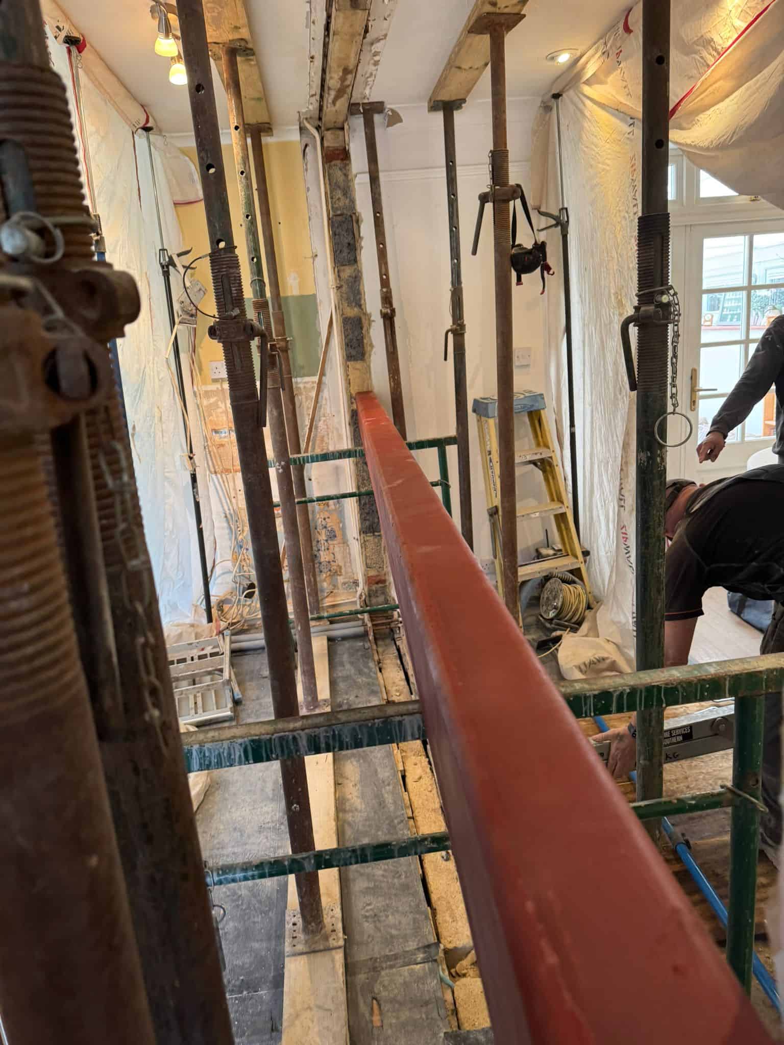 Interior view of house extension construction with scaffolding and building materials.