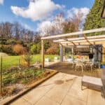 Outdoor patio with glass conservatory extension and lush garden backdrop.